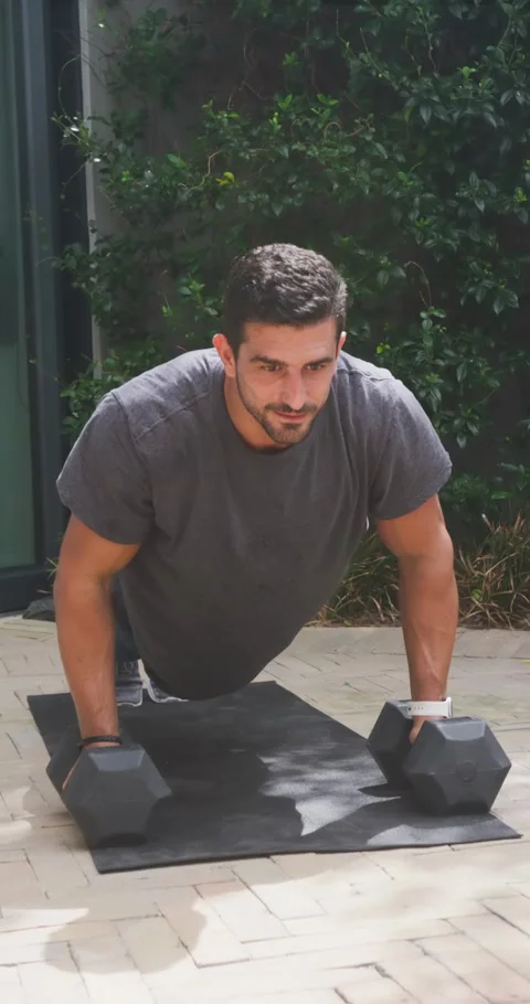 Man starting lowered chest on mat, doing push-ups using hex dumbbells on patio Stock Footage 345130664