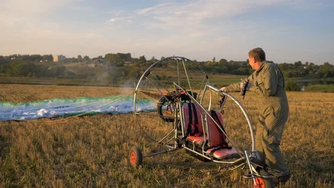 The man starts the engine of the powered paraglider on the field Stock Footage 94400611