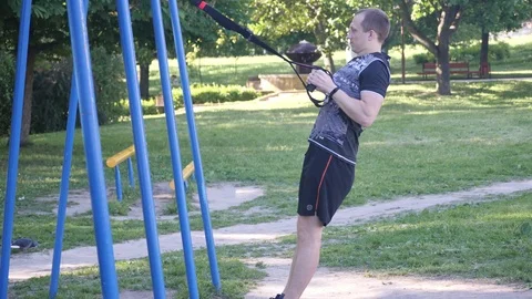 Man starts intense pull-up exercising with fitness loops in a park. 4K slow mo Stock Footage 99314566