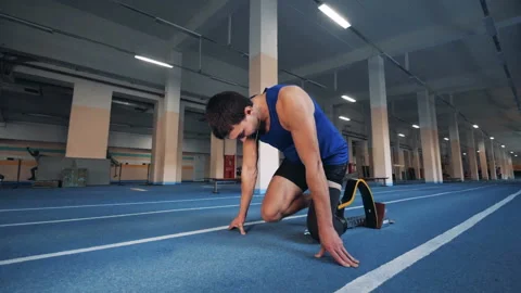Man starts to run on a track, wearing artificial leg, side view. Video stock 100833530