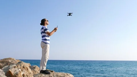 Man stay on stone with controller, send drone to flight over beautiful sea Stock Footage 105199209
