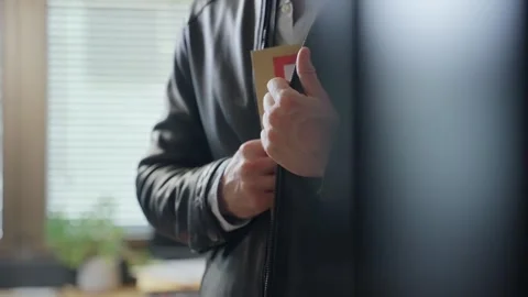Man stealing and hiding top secret file folder in leather jacket inside office Stock Footage 304407353