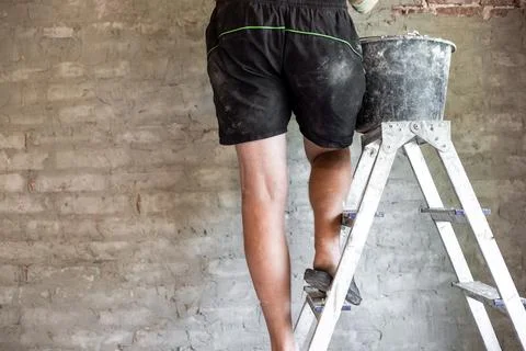 A man on a stepladder plasters an old brick wall with a cement-sand mixture Foto stock