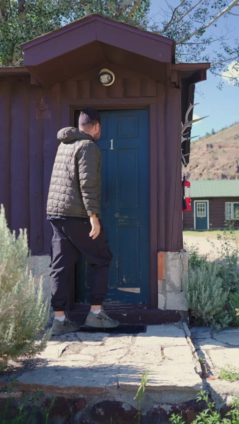 A man is stepping out of a rustic cabin that is surrounded by a beautiful scenic Stock Footage 315614804