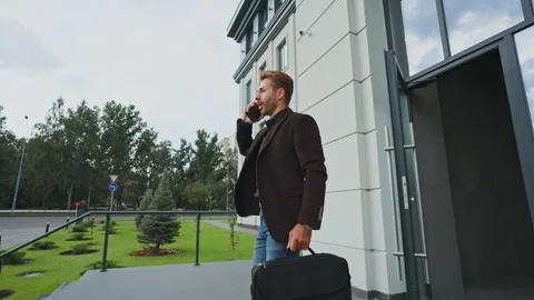 Man steps outside a modern building while checking his smartphone during the day Stock Footage 288184406