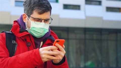 Man in sterile protective mask using his phone on street and looking to camera Stock Footage 129939916