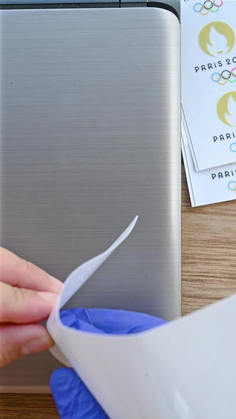 Man sticking a label of Paris Olympic Games 2024 logo to a laptop vertical Stock Footage 244773293