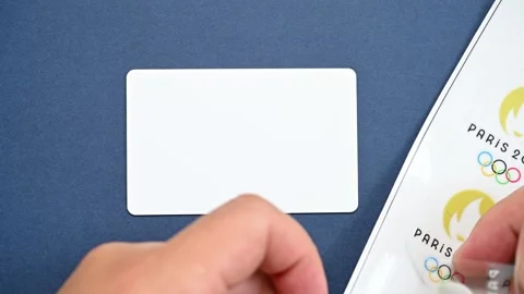 Man sticking a label of Paris Olympic Games 2024 logo to a blank IC card Stock Footage 250602255