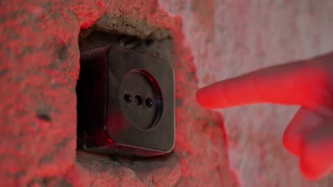 A man sticks his finger into the socket under red lighting close-up. Old room Stock Footage 202645004