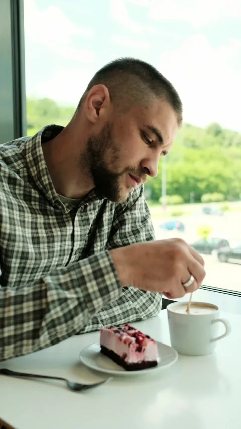 Man stirring a cup of coffee next to a slice of berry cheesecake in a cafe Stock Footage 316144371