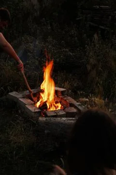 A man is stirring a large fire using a long wooden stick carefully Stock Photos