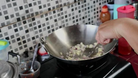 A man is stirring shallots and garlic into a wok to season fried rice. Stock Footage 242569602
