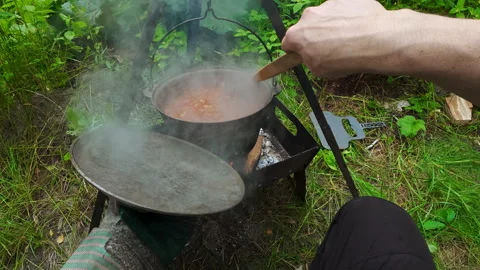 Man stirring steaming stew in campfire cauldron for outdoor picnic cooking .. Video stock 342595411