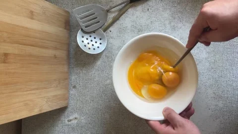 Man stirs and beats egg yolks with fork in white bowl on gray table Stock Footage 277173182