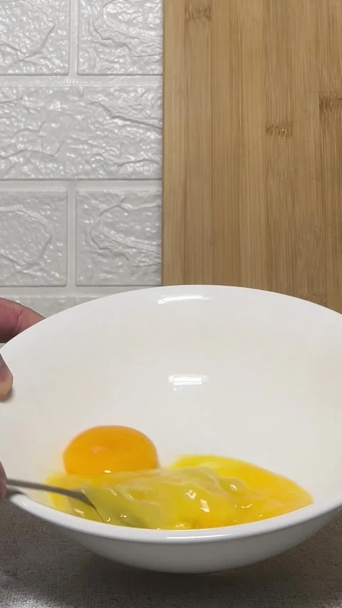 Man stirs and beats egg yolks with fork in white bowl on gray table Stock Footage 280482388