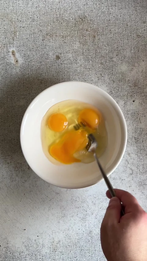 Man stirs and beats egg yolks with fork in white bowl on gray table Stock Footage 282557170