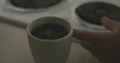 Man stirs hot cup of tea in dark kitchen 库存影片 78038324