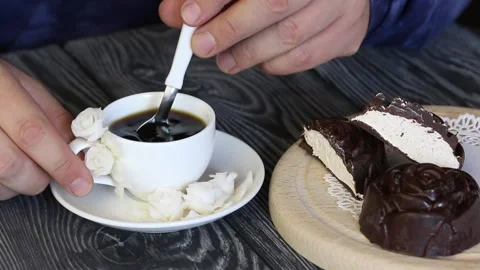 A man stirs a spoonful of sugar in a cup of coffee. Nearby lies a marshmallow Stock Footage 135270715