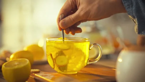 A man stirs a steaming citrus tea infused with fresh lemons and ginger in a Stock Footage 334075578