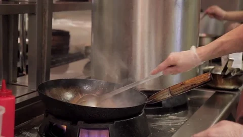 Man stirs vegetables and meat on hot frying wok pan in kitchen in restaurant. Vidéo 76476100