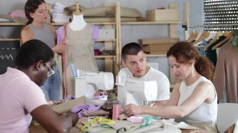Man stitching on machine and talking with classmate in sewing class Stock Footage 341430040