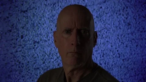 A man with a stoic expression in front of a TV screen with noise and static Stock Footage 234427835