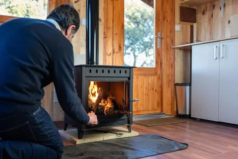 Man stoking the fire in a rustic cast iron fireplace to heat the house in winter Stock Photos
