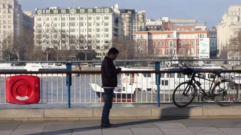 Man stops walking to text besides River Thames Stock Footage 46222569