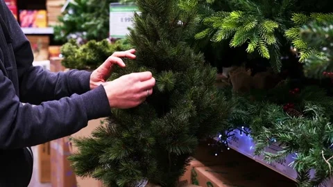 A man in a store chooses an artificial fir tree for Christmas 스톡 동영상 225487217