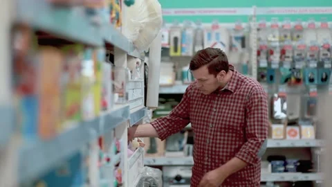 A man in a store chooses a small ukulele guitar trying to play it. Stock Footage 131440983