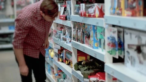A man in the store chooses a toy small tank examines it. Stock Footage 131375223