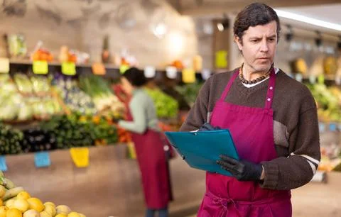 Man store employee with folder of documents takes inventory in vegetable store 写真素材