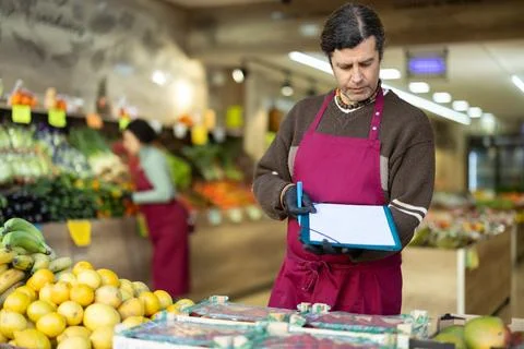 Man store employee with folder of documents takes inventory in vegetable store 写真素材