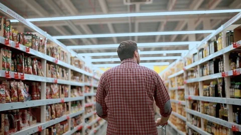 A man in a store goes with his back with a trolley chooses goods Stock Footage 126865740