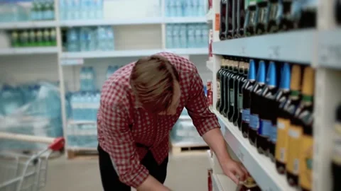 A man in a store takes a large bottle of beer from a shelf and puts it in a cart Stock Footage 131461060