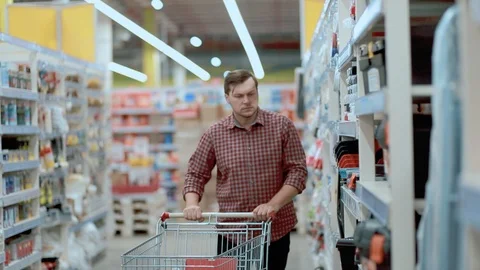 A man in a store with a trolley selects goods in a plaid shirt Stock Footage 126279200