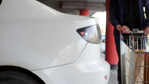 A man stores parcels from a store in the trunk of a car in the parking lot. A 스톡 동영상 129258925
