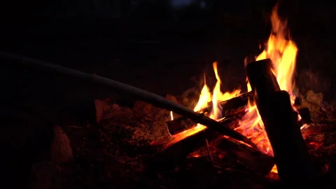 The man straightens the coals in the fire. The fire is burning in the middle of 库存影片 136438222