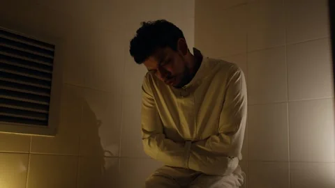 Man in Straitjacket Sitting Alone in Dim Cell Under Low Light Stock Footage 325022408