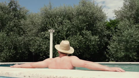 Man in straw hat relaxing in water of luxury swimming pool against background of Stock Footage 296803615