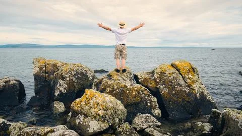 Man in straw hat standing on the rocks by the ocean, adventure lifestyle concept Stock Photos