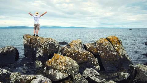 Man in straw hat standing on the rocks by the ocean, adventure lifestyle concept Stock Photos