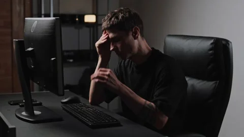 Man stressed at computer desk feeling overworked and exhausted in dark office Stock Footage 317944227