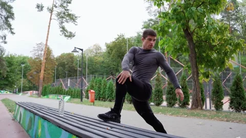 A man is stretching on a bench in the park under Stock Footage 265399956