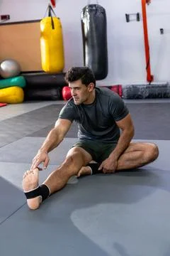 Man stretching hamstring on martial arts mat in studio with hanging punching Stock Photos