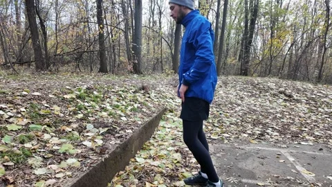 Man stretching leg on outdoor step in autumn park, warming up before training Stock Footage 318166069