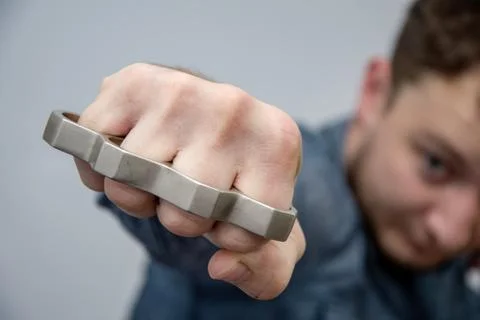 Man strikes brass knuckles on a light background, a prohibited weapon in a fight Фото