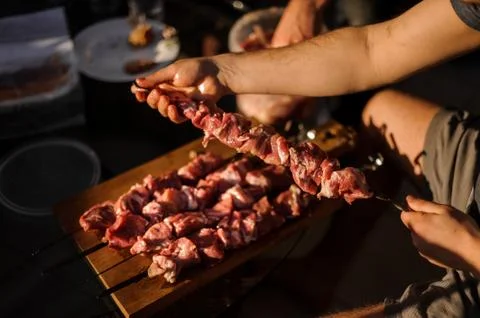 Man string meat pieces on the skewer and place them to the cutting board 스톡 사진