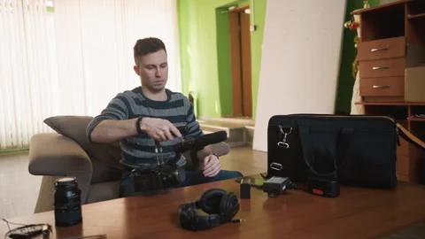 Man in striped sweater reaching for camera equipment bag, surrounded by camera Stock Footage 317546637