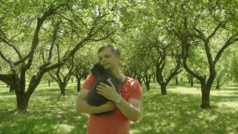 Man Stroking a Cat and walks through green trees alley. Stock Footage 110789356